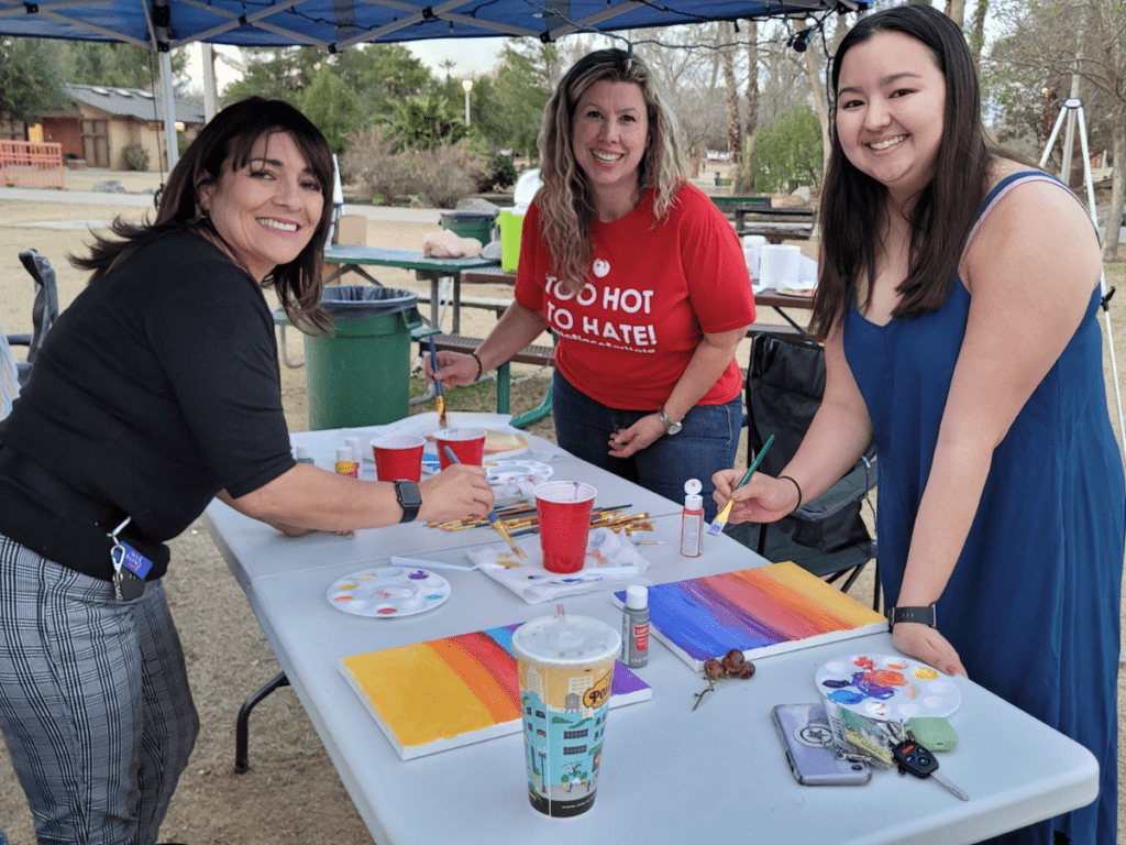 Three women smiling as they paint canvases in the park