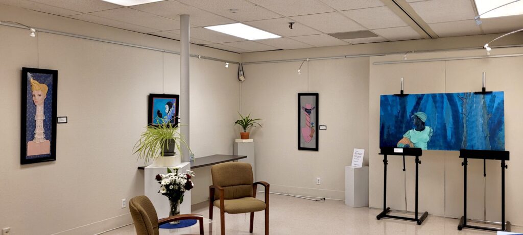 A panoramic photo of the Larry Wilson Gallery space. A room with white walls that has art hanging on them, there are flowers and potted plants on pedestals and two chairs in the middle of the room. 