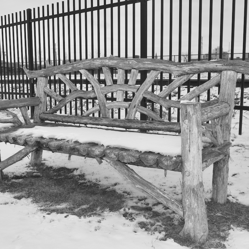 A photograph of a snow covered wooden bench taken in black and white.